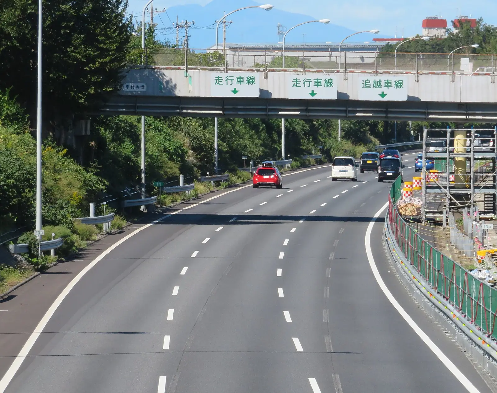 A multi lane Japanese expressway with overhead lane signage in Japanese, traffic keeping to the left