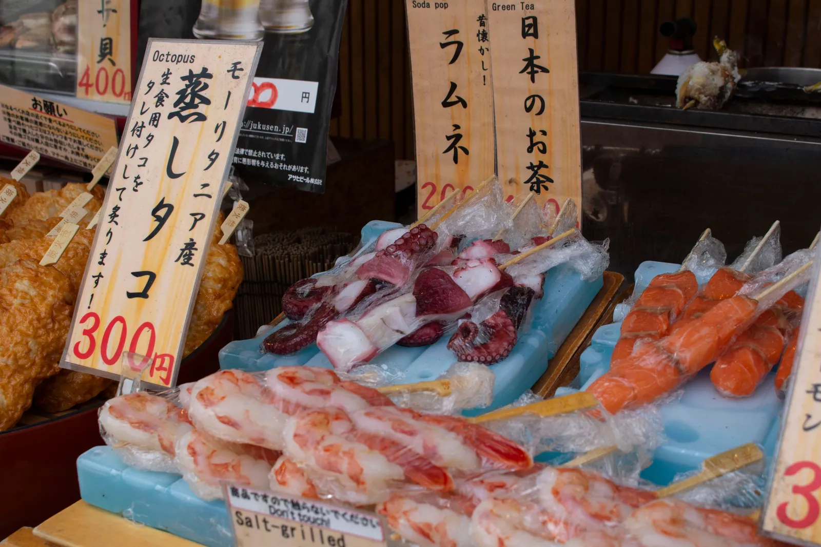 Steamed octopus and seafood skewers on ice at a market food stall in Kansai, Japan, with handwritten Japanese price signs