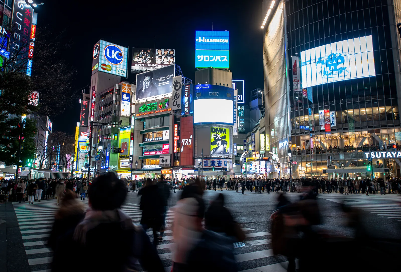 A busy pedestrian crossing surrounded by illuminated screens and buildings in central Tokyo at night, Japan