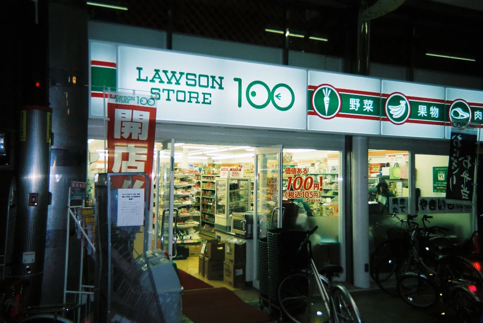 חזית חנות קומביני 7-Eleven מוארת בלילה ברחוב ביפן עם מדפי אוכל מלאים ושלטים בכתב יפני