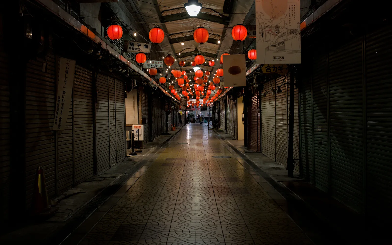 An empty covered shopping arcade in Japan with the shops shuttered and red lanterns lit