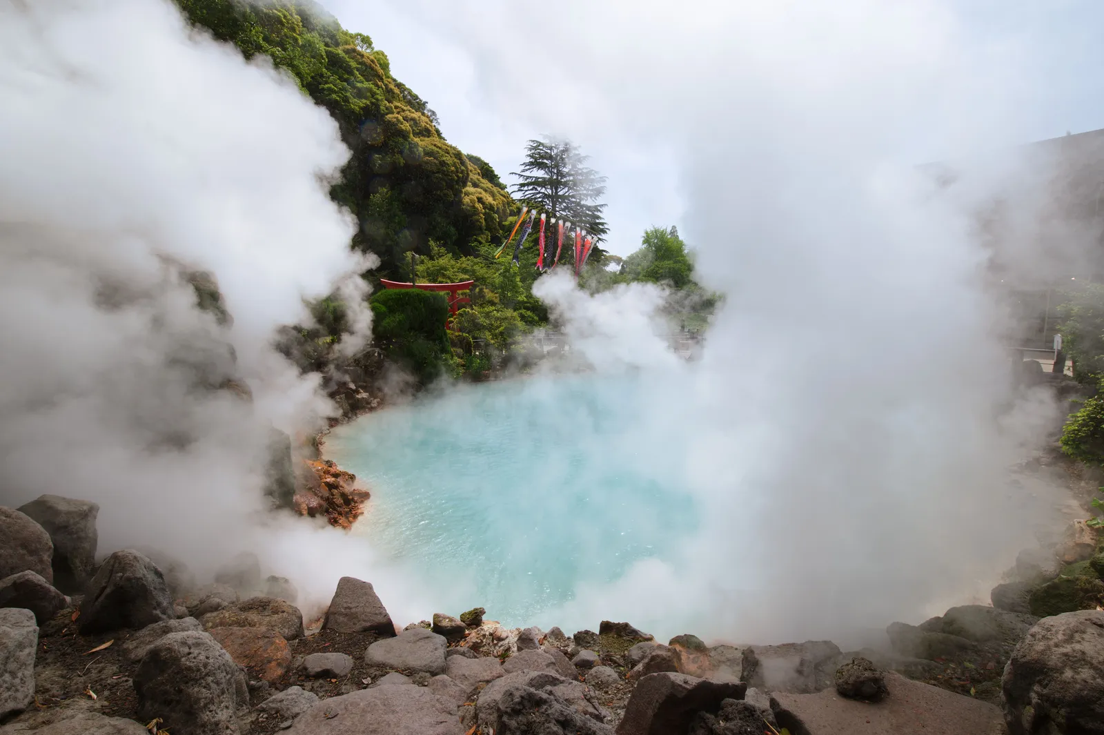 A steaming milky blue hot spring pool among rocks with thick vapour rising in Japan
