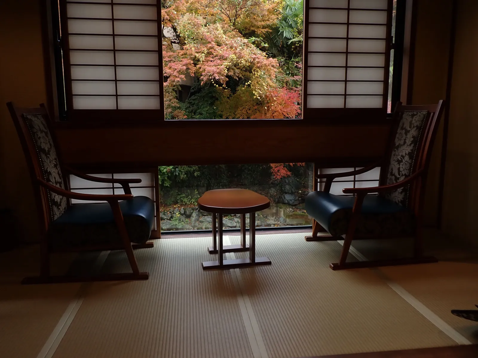A tatami room in a Japanese inn with two low chairs and a window looking out onto autumn maples