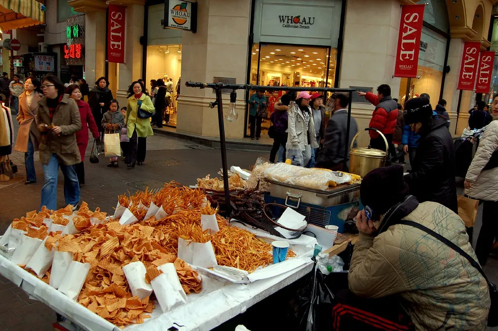 A busy street food and shopping street in Myeongdong, Seoul, lined with stalls and signs