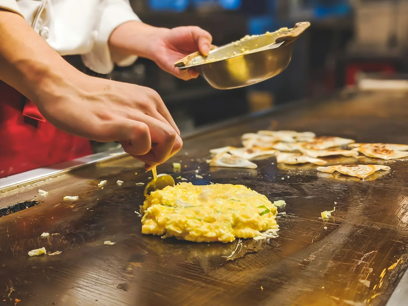A chef griddling okonomiyaki pancakes on a hot plate in an Osaka restaurant