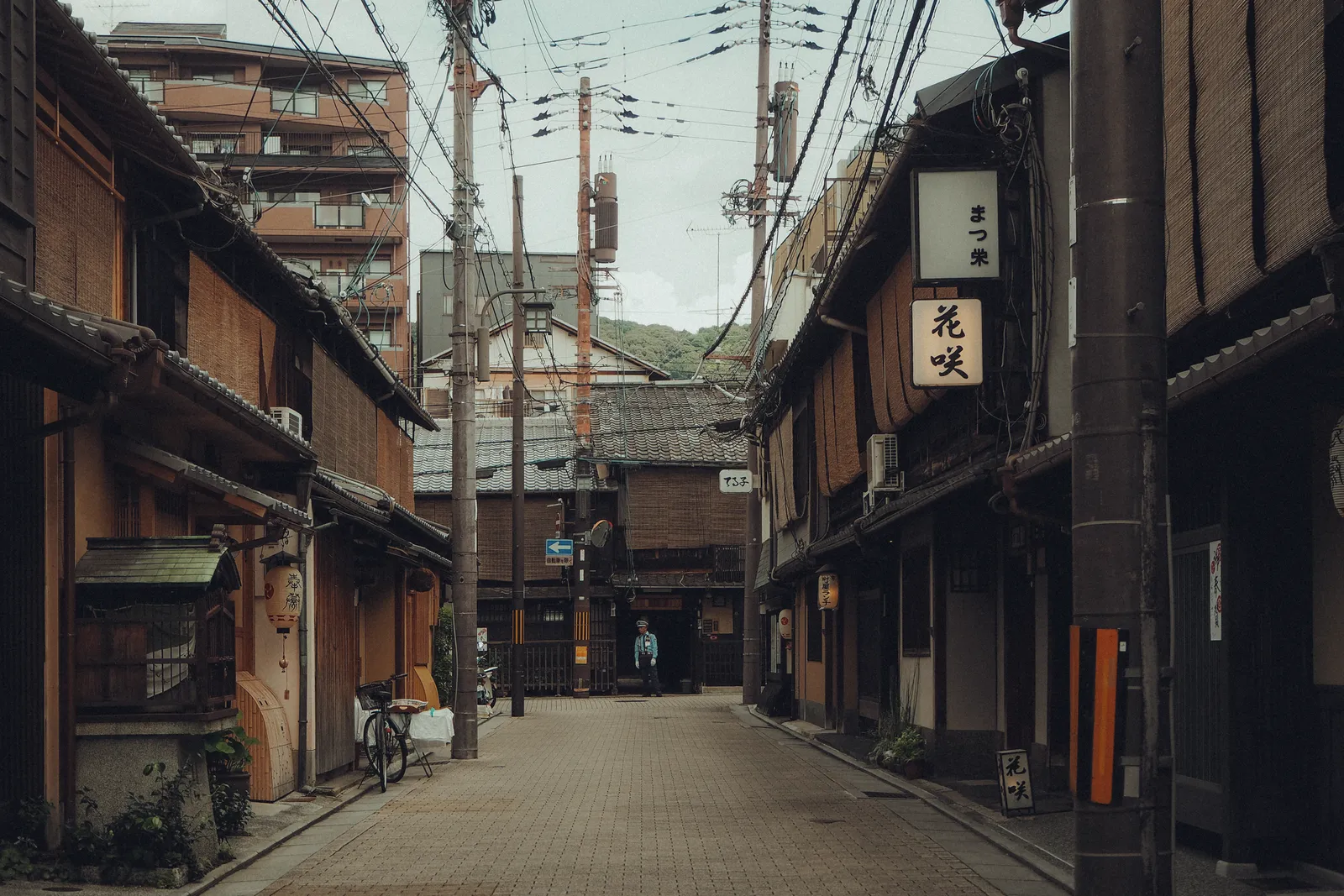 A quiet narrow street of wooden machiya townhouses with a hanging shop lantern in Kyoto, Japan