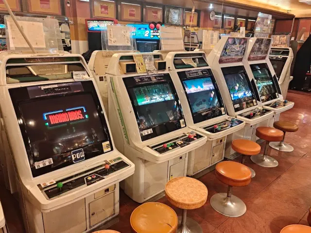 A row of old arcade game machines with orange stools on a reddish floor