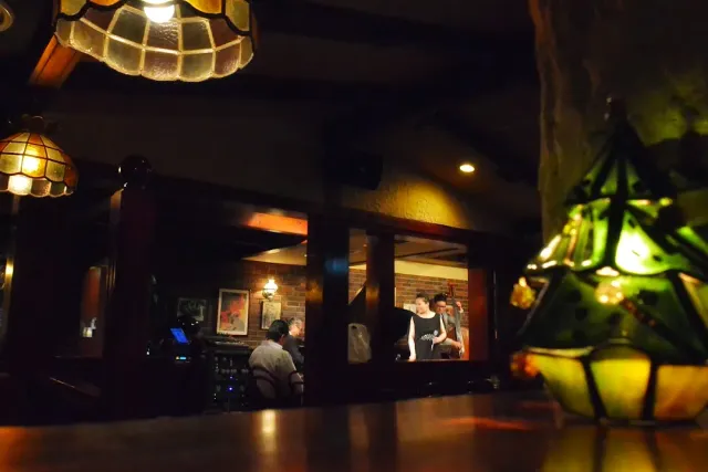 A dark space with green stained glass lamps, wooden columns and people at tables