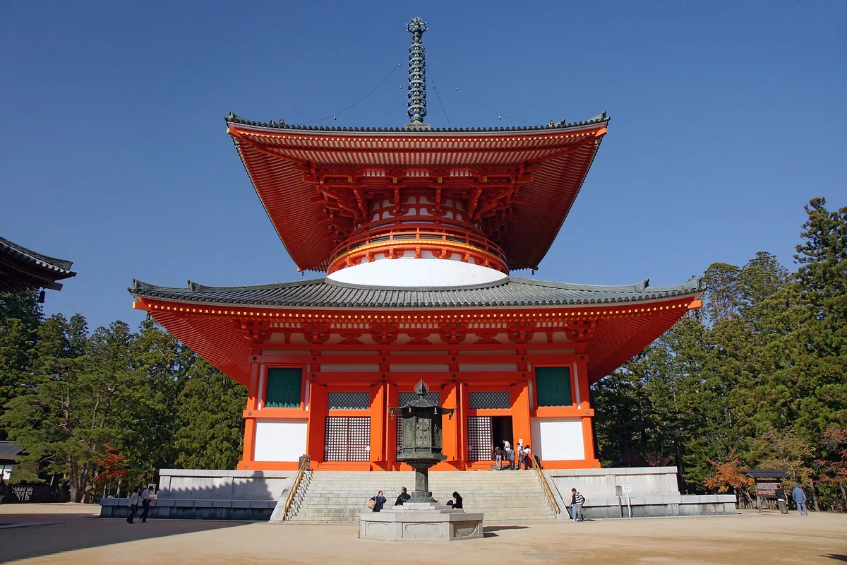 The tall red Konpon Daito pagoda at the Danjo Garan temple complex in Koyasan, on a clear day surrounded by green trees