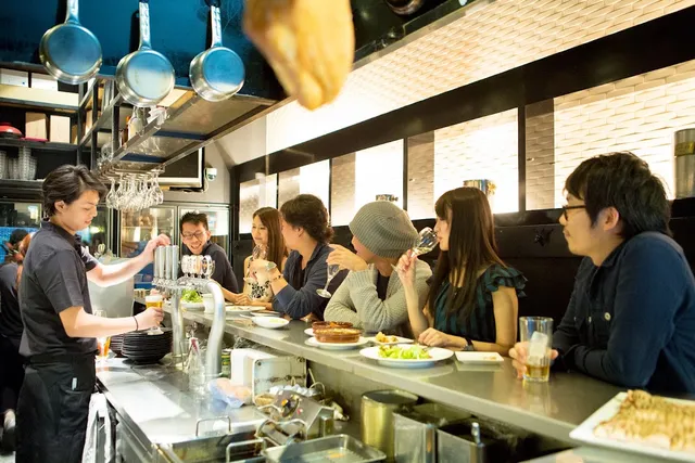 Diners sitting along a counter with glasses and dishes, facing staff pouring drinks