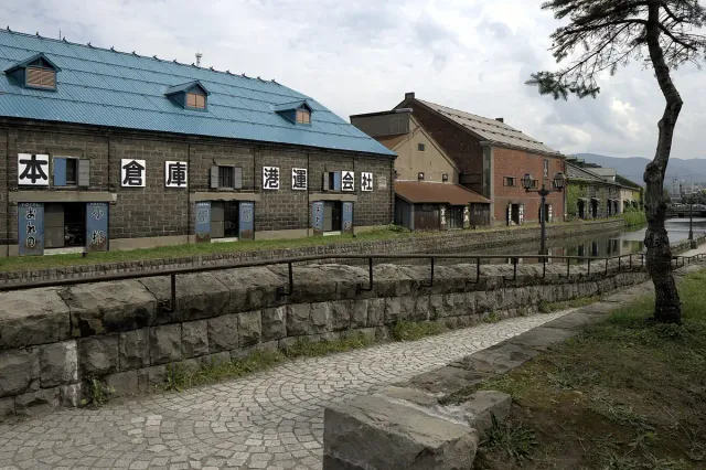 Stone canal beside a long wooden warehouse with a blue roof, empty promenade