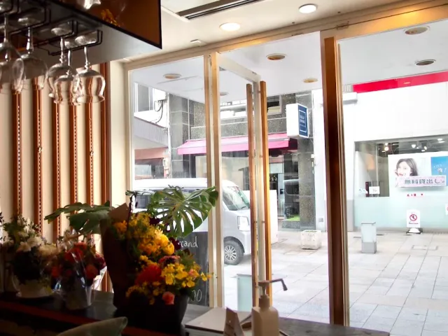 A view from inside toward the street through a glass door, with flower vases and hanging glasses