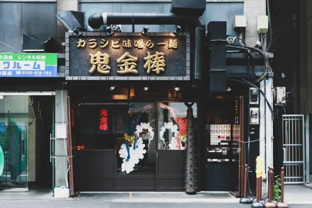 A dark frontage with a large gold sign, colourful figure decorations and a ticket machine at the side