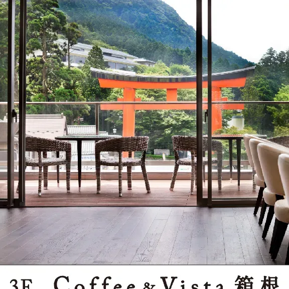 A terrace with wicker chairs facing a large red gate, with green hills in the background