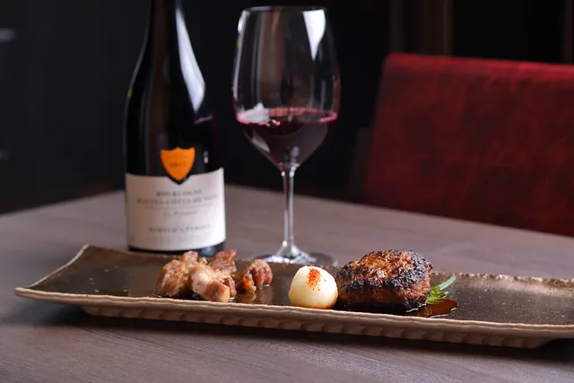 A platter of grilled meat pieces beside a bottle of wine and a glass of red wine