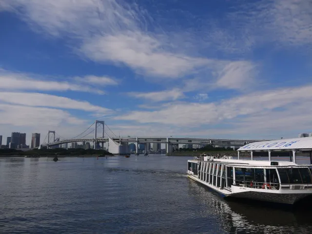 A water bus moored at a pier, a suspension bridge and skyline behind
