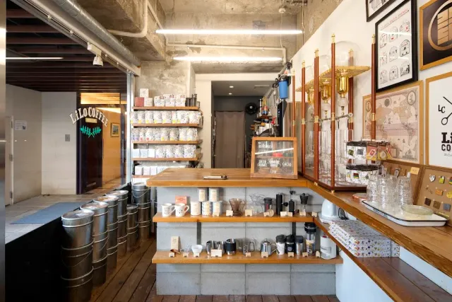 A narrow space with a wooden counter, metal canisters on the floor and a neon sign above a dark door
