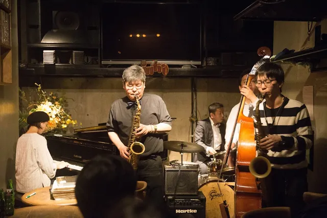 A jazz group playing in a small room, with saxophone, double bass, drums and piano