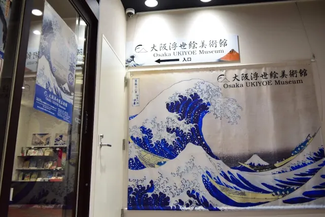An entrance with a large curtain printed with a blue wave, and an arrow sign above it