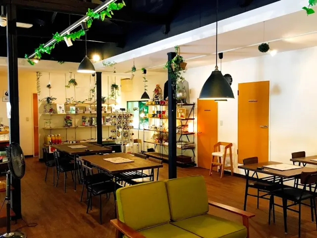 A space with wooden tables, a green sofa, shelves of products and plants hanging from the ceiling
