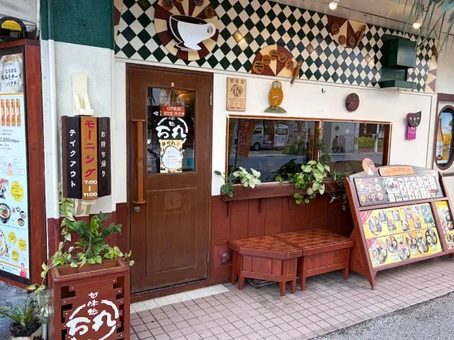A small front with a diamond patterned wall and a cup drawing, a wooden door, benches and a photo menu sign