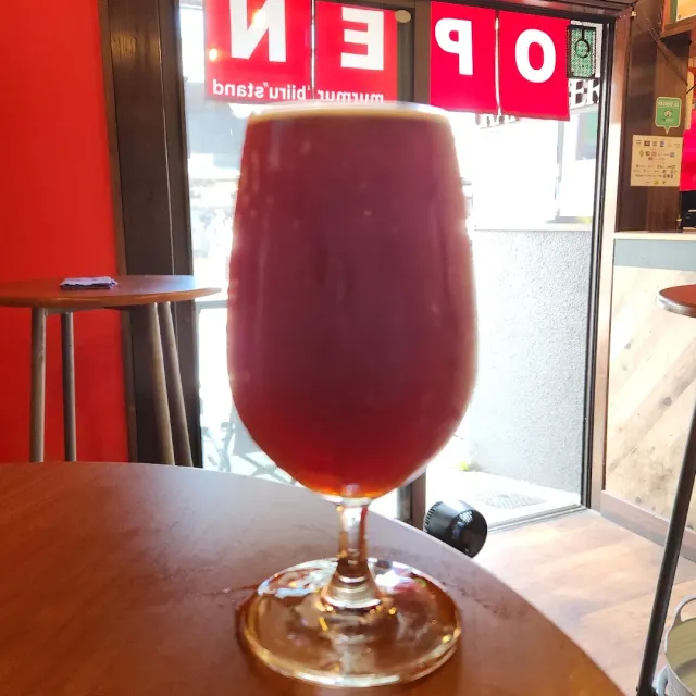 A glass of reddish beer on a wooden table facing a red sign in the window