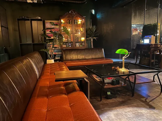 A long brown leather sofa around a glass table, a green desk lamp and bookshelves