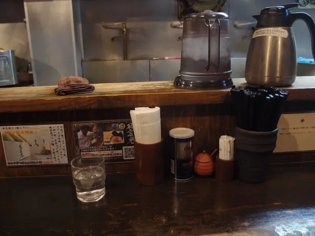 A narrow wooden counter with a water glass and condiment jars