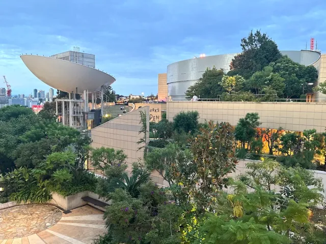 A green roof with shrubs and paths, rounded buildings and a skyline at dusk