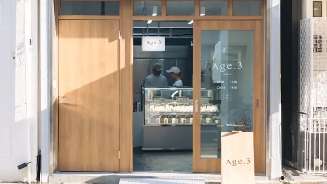 A storefront with light wooden doors, a chilled display case and two staff behind it