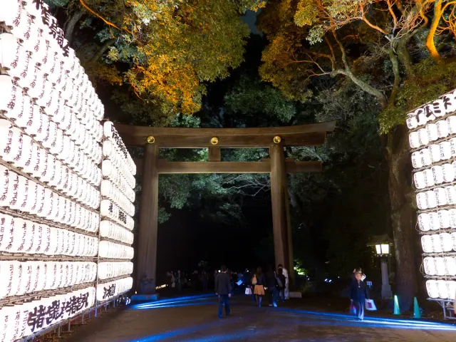 A wall of white paper lanterns beside a large wooden gate, trees around