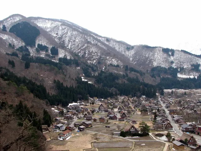 A village in a snowy valley at the foot of a forested mountain