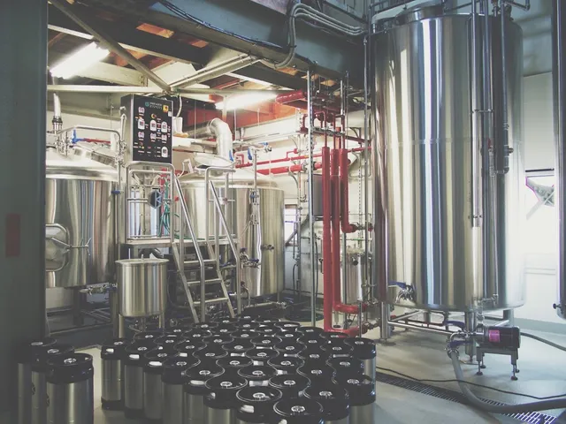 Stainless steel brewing tanks, red piping and rows of small kegs on the floor