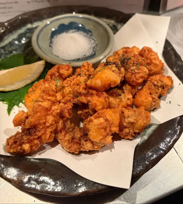 Crispy fried chicken on paper in a dark dish, with salt and a lemon wedge