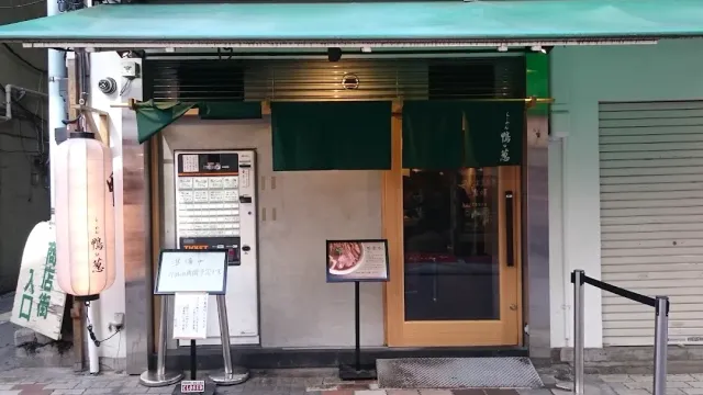 A small frontage with a green awning, a green fabric curtain, a ticket machine and a white lantern