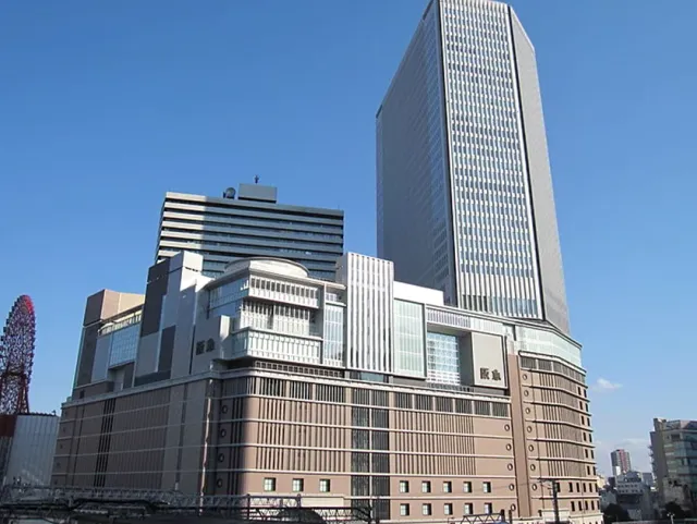 A large commercial building with a glass office tower behind it, under a blue sky