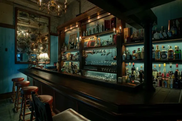 An antique back bar with bottles and glasses, a chandelier and upholstered stools