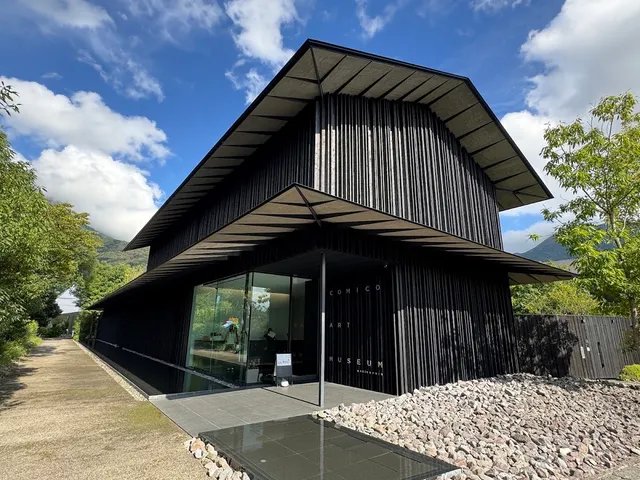 A modern building clad in dark wood with a sloping roof, a glass front and a bed of stones
