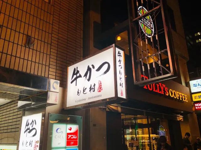 An illuminated projecting sign with Japanese script on a building wall, on a street full of signs at night