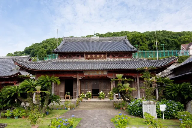 A double roofed Chinese style temple hall, surrounded by palms and hydrangea bushes in the garden