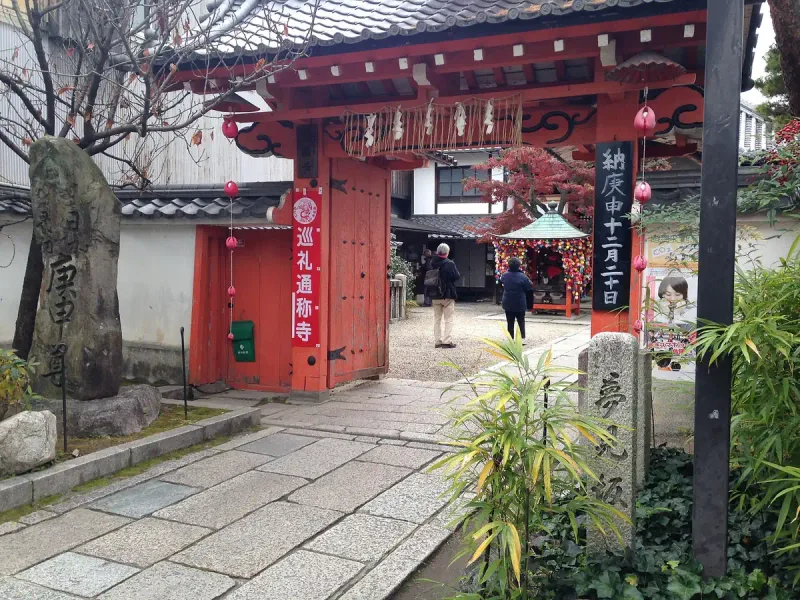 Red temple frontage on a narrow Kyoto lane, with colourful cloth balls and visitors on the stone path
