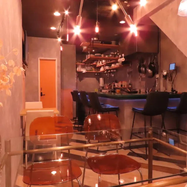 A room with a bar and tall stools, orange transparent chairs and warm bulb lighting