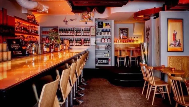 A long lit counter with wooden stools and shelves of whisky bottles along the wall