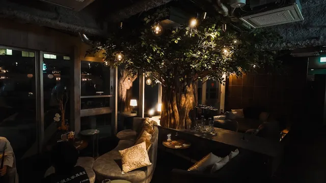 A dim space with a large tree in the centre, hanging bulbs and sofas with cushions