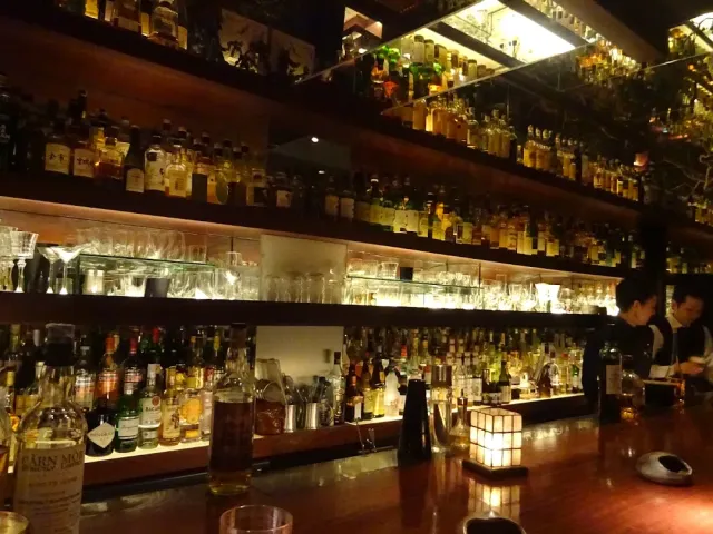 Lit shelves with hundreds of whisky bottles above a glossy wooden counter