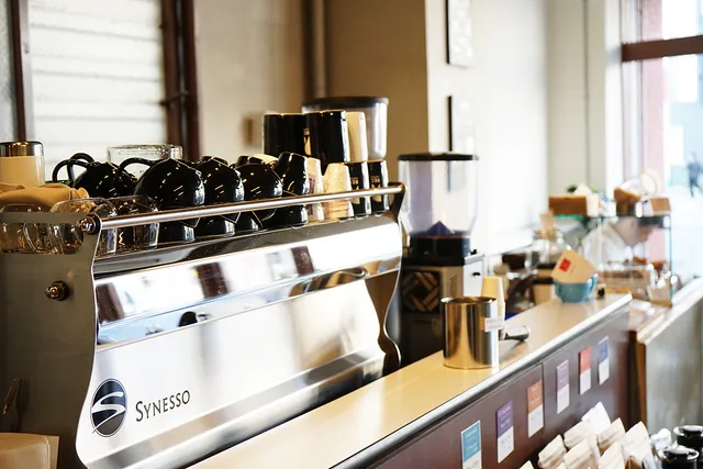 A stainless steel espresso machine with black cups on top, beside a coffee grinder