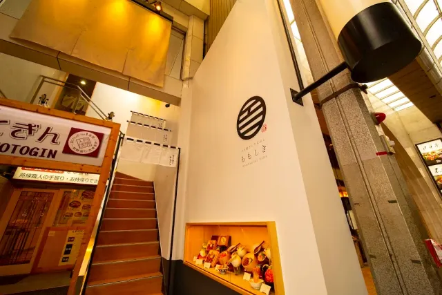 A lobby with a wooden staircase, a round emblem on a white wall and a lit display case with products