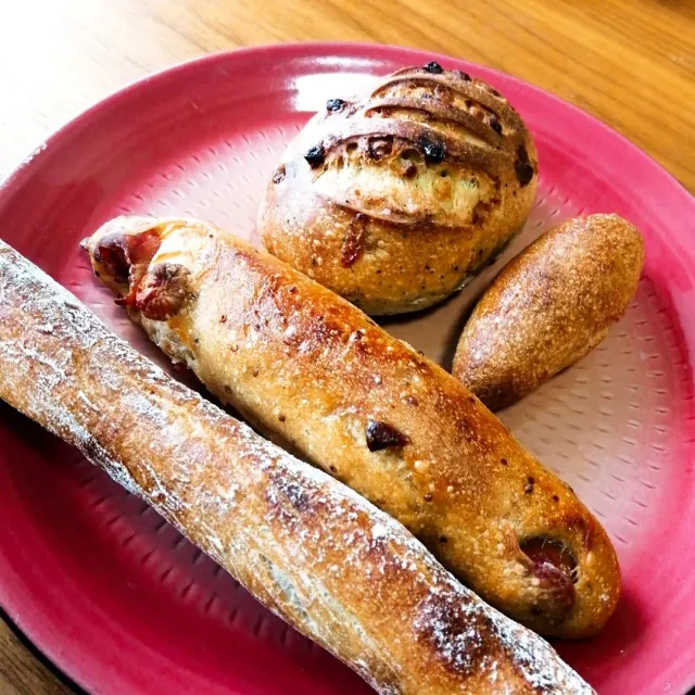 A red plate with three baked breads, among them a long loaf and a round roll