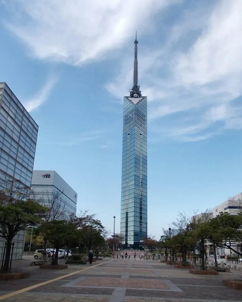 Triangular glass clad observation tower above office blocks under a blue sky
