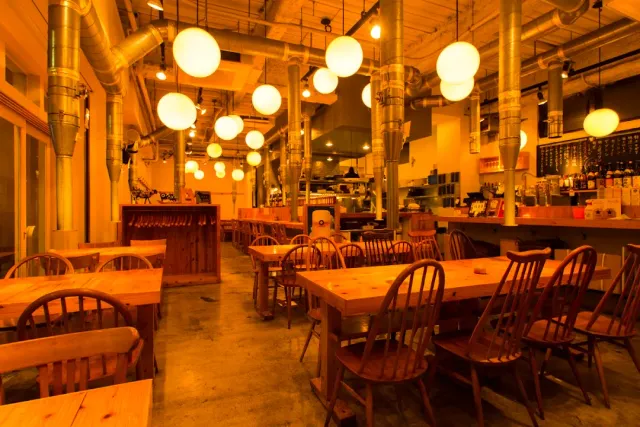 A large warmly lit hall with globe lamps, wooden tables, chairs and extraction pipes